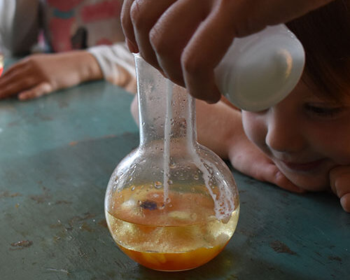 Dete radoznalo posmatra naucni eksperiment u kome se tecnost sipa u staklenu tikvicu