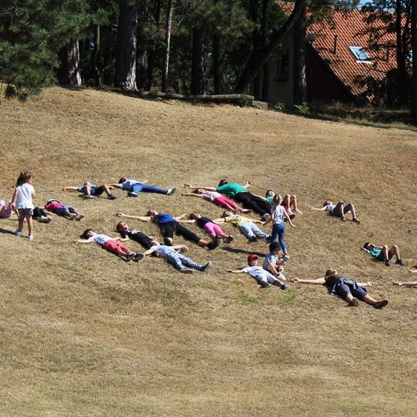 Deca i nastavnici opusteno leze rasirenih ruku i nogu na poljani