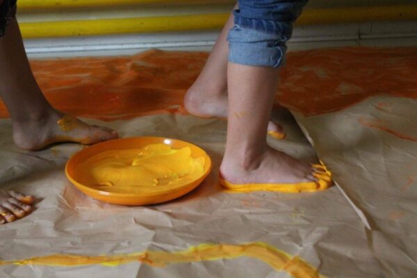 Decja stopala ostavljaju trag od zute boje na papiru na podu