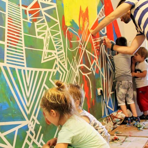 Deca prave umetnicko delo na zidu u zelenoj, zutoj, plavoj i crvenoj boji sa belim trakama